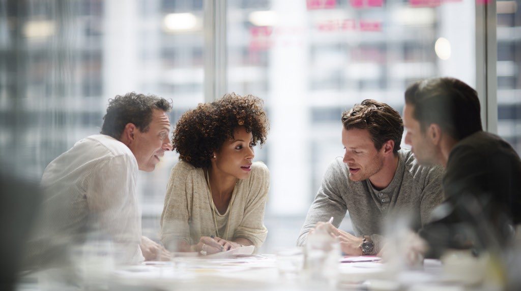 Four professionals collaborating around a table with papers in a bright office overlooking the city