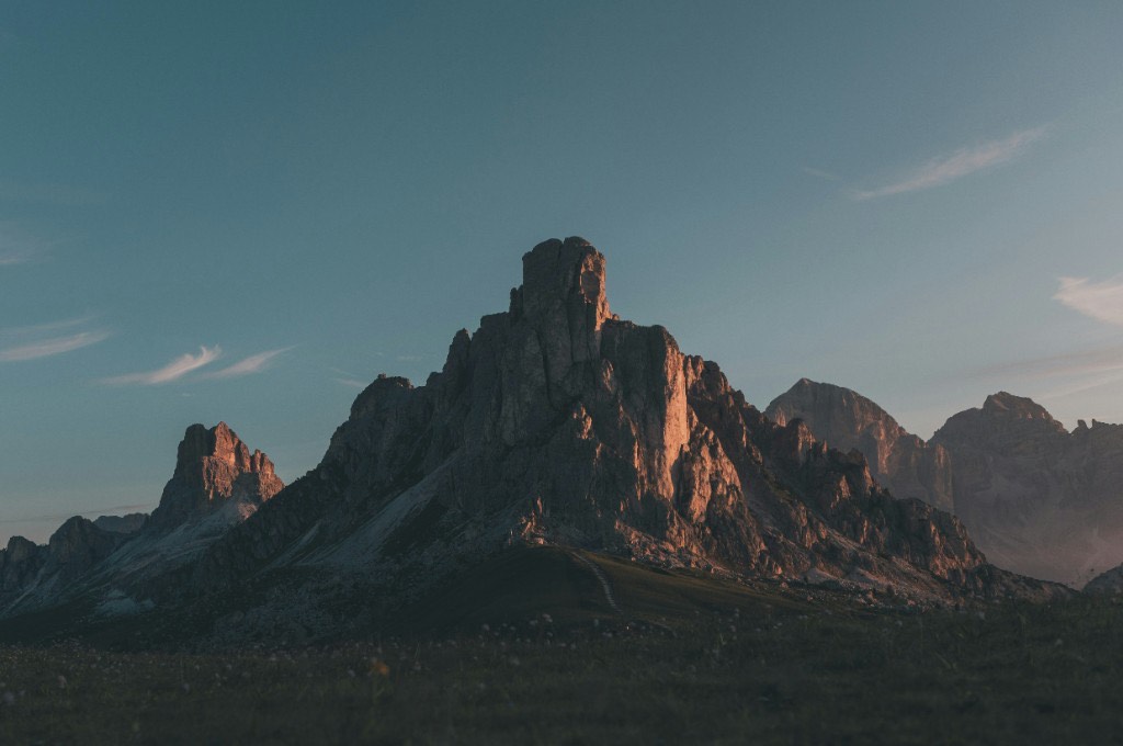 Sunlit mountain peaks at dusk with a dark meadow in the foreground
